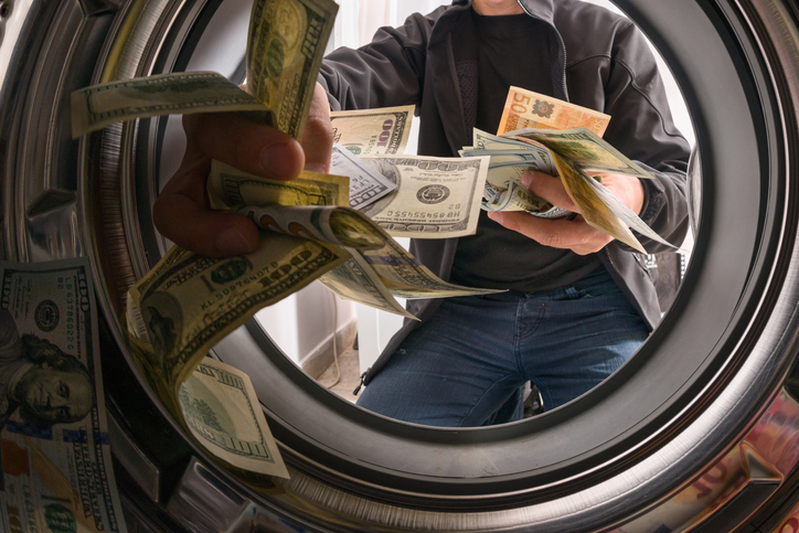 A man throwing cash into the washing machine to represent money laundering.