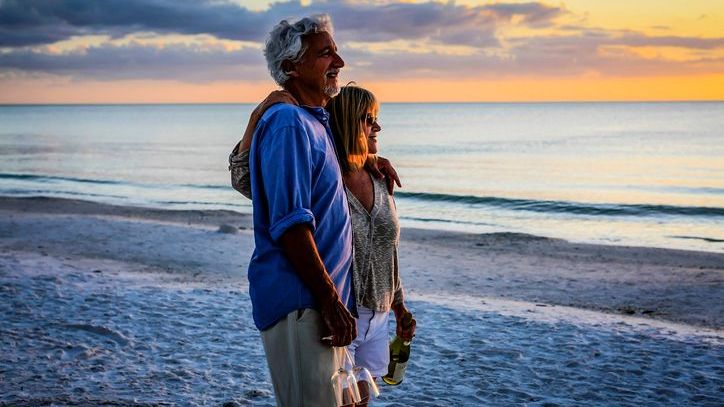 A couple celebrates their retirement together on a Florida beach with a bottle of champagne.