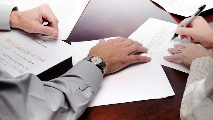 A woman signs a codicil while sitting next to another person.