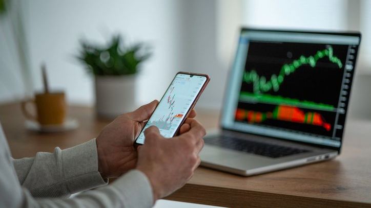 A person examines price charts on their smartphone and laptop.
