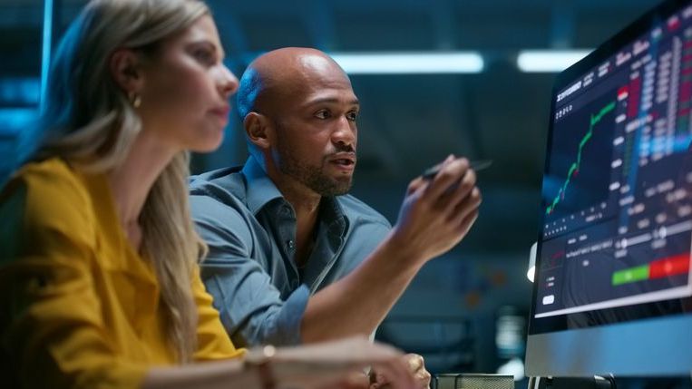 Colleagues review financial data on a computer screen.