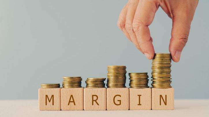 A word "margin" is spelled out on wooden blocks while a hand stacks coins on top of them.