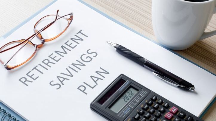 A pair of glasses, a pen and a calculator all rest on top of retirement savings plan documents.