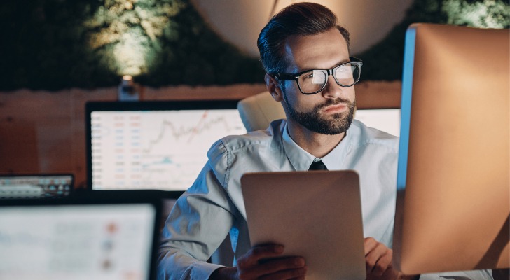 A man confidently looks over data on several screens in an office.