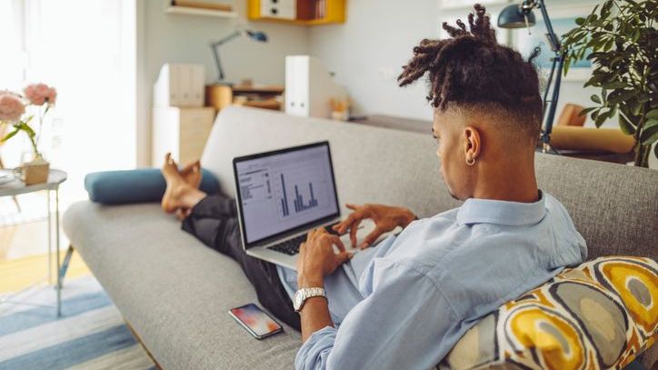 A man reviews data on his computer while sitting on his sofa.