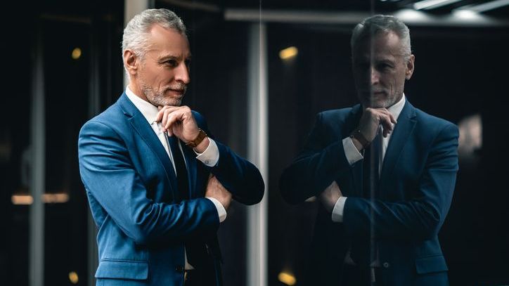 A man in a suit looks at his reflection in a window.