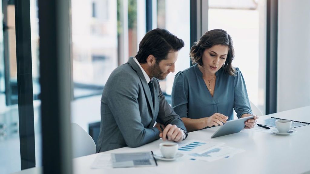 A man and woman look over data on a tablet.