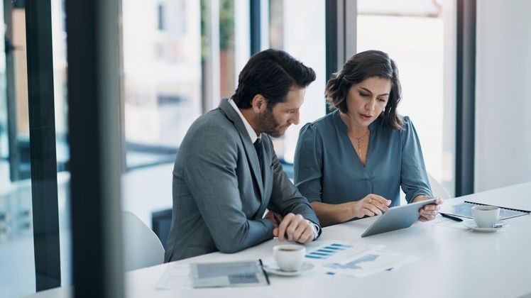 Colleagues go over financial data on a tablet while siting together at a conference table.