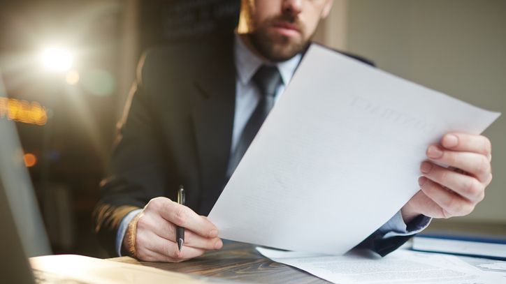 A closeup of a bearded businessman holding papers in his hands.