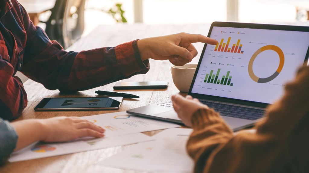 Three colleagues huddle around a tablet during a meeting.