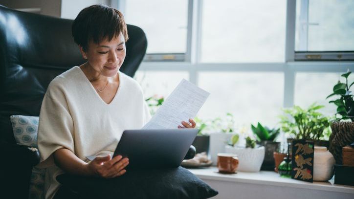 A woman sits in a chair and looks over expenses on her tablet.