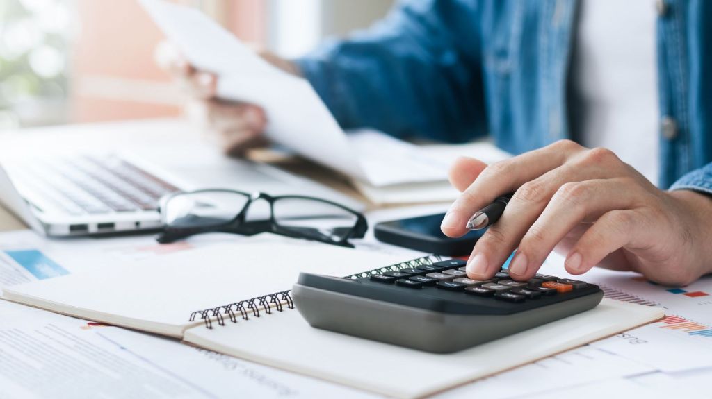 A closeup of a person using a calculator while reviewing paperwork.