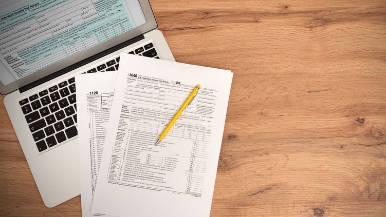 A pen and IRS tax forms on top of a laptop computer keyword.