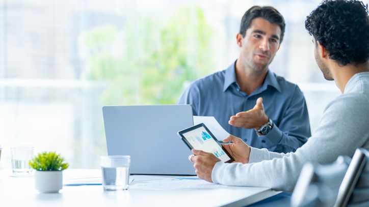 Two businessmen working on a digital tablet and laptop computer in an office.