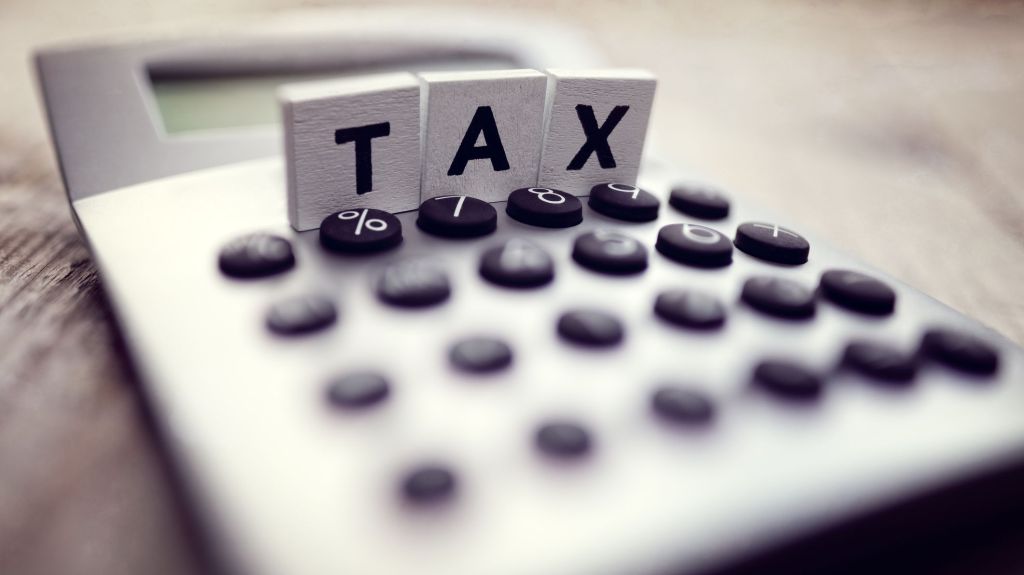 A closeup image of a calculator with the word "tax" written in wooden block letters.