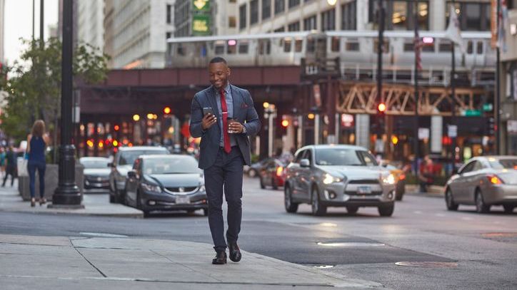 A smiling Chicago businessman using his phone while walking away from an L train.