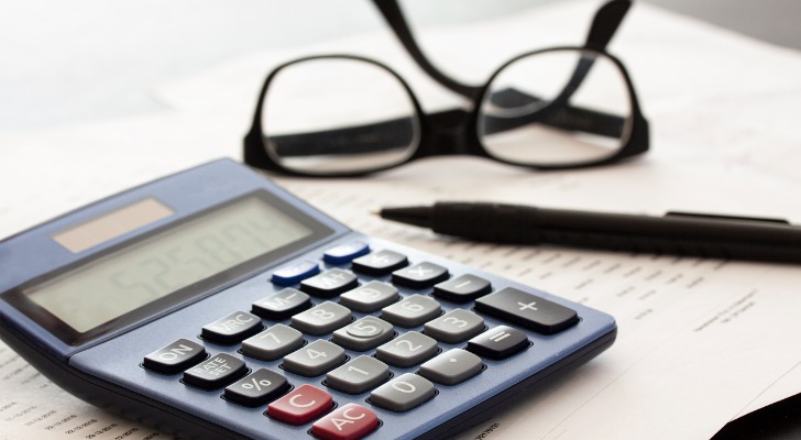 Closeup of a calculator, glasses and a pen resting on top of a note pad.