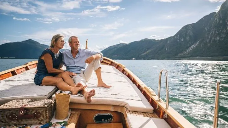 A couple enjoys the sunshine while sailing on a lake surrounded by mountains.
