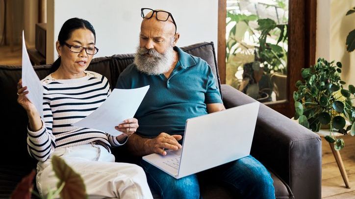 A middle-aged couple reviews their retirement plan while sitting together on a couch.