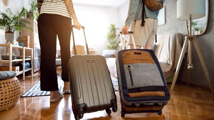 A rear view of an unrecognizable couple arriving at their accommodations with their suitcases.