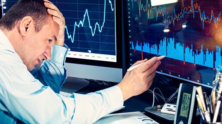 A stressed economic clutches his forehead as he analyzes charts on a computer monitor.