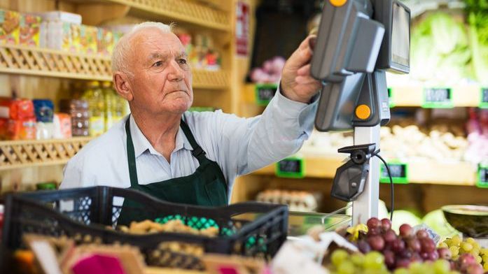 A senior man working as a cashier at a grocery store.