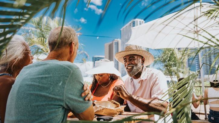 Two couples in their 60s sit at a picnic table together at a food fair in Hawaii.