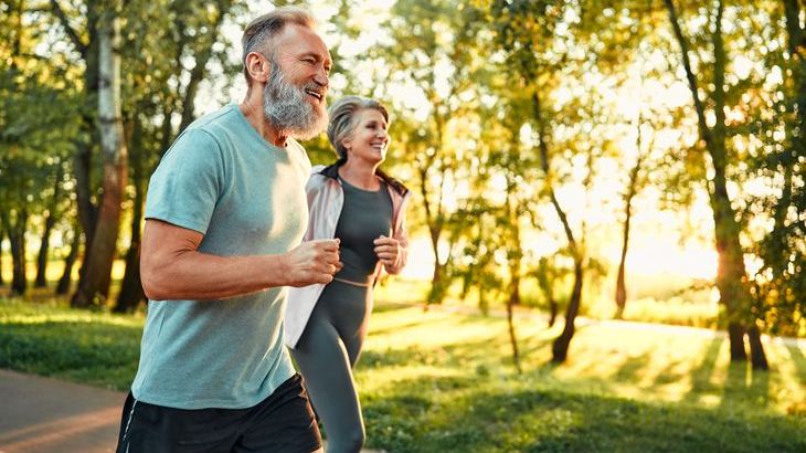 A man and woman in their 60s running together in a park.
