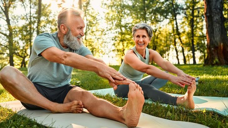 A retirement-age couple stretches on yoga mats in a park.
