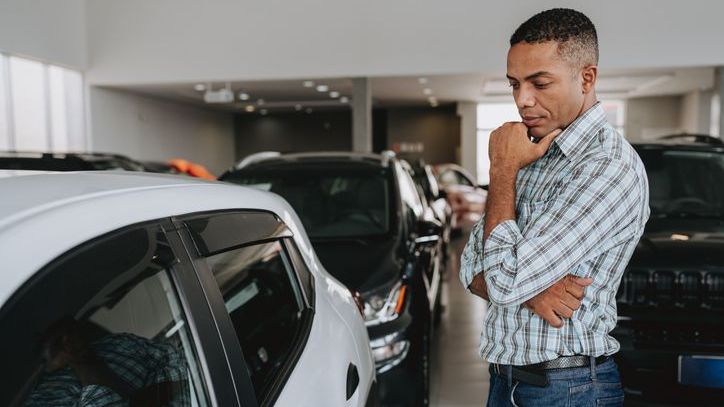 A man stands inside a car dealership and contemplates the price of a vehicle.