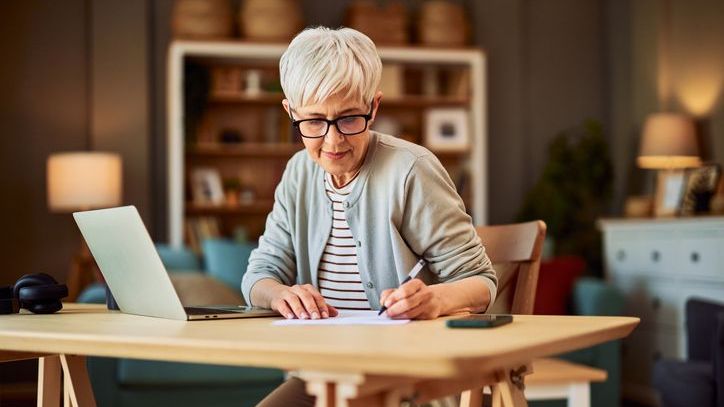 A senior female accountant with reading glasses working from home.