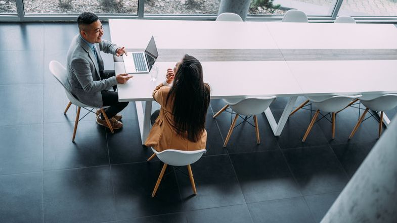 An aerial view of man and a woman sitting at a long conference table discussing business strategy.