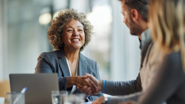 A woman in a suit jacket smiles as she shakes with a man during a business meeting.