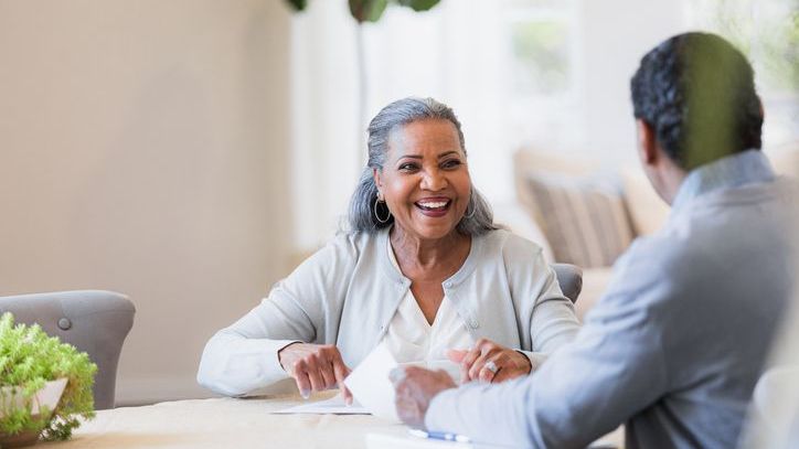 A woman in her 60s smiles during a meeting with her financial advisor at home.