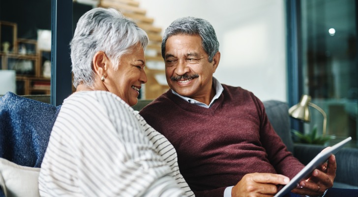 A man and woman who appear to be in their 60s or 70s smile while reviewing information on a tablet.