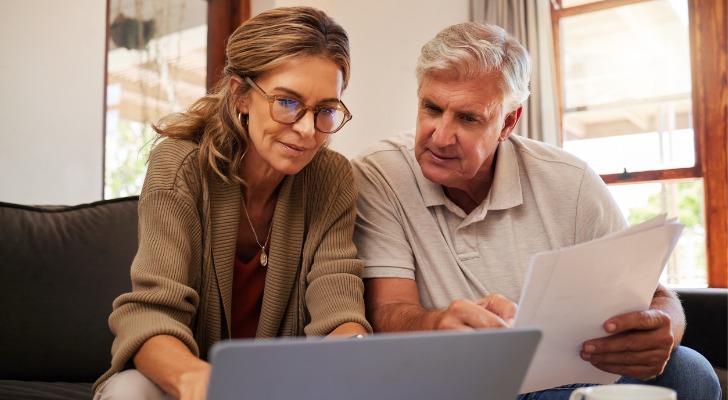 A senior couple reviewing a retirement budget together at their kitchen table, with notes and a laptop open to financial planning charts.