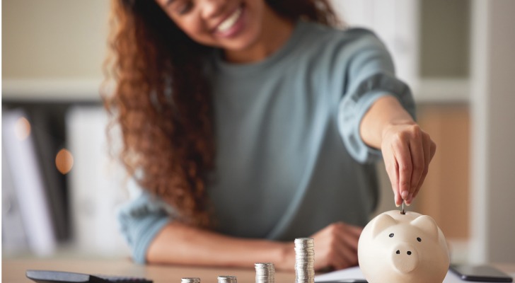 A woman putting coins into a piggy bank, symbolizing the importance of saving for retirement.