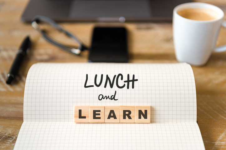 A notebook reading "lunch and learn" in front of a laptop and cup of coffee.