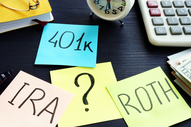 Pieces of paper labeled 401(k), IRA, and Roth scattered on a desk, symbolizing retirement planning.