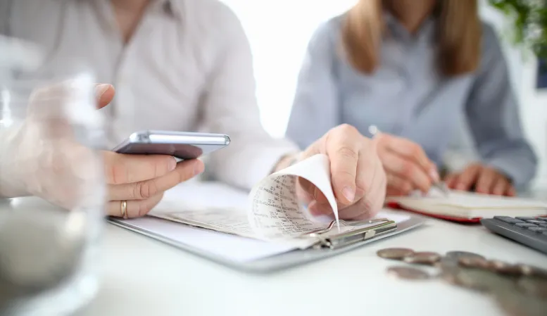 A couple checking their taxes using a mobile smartphone app against the background house.