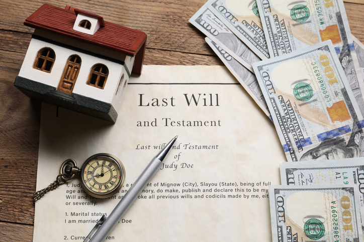 Top view of a last will, pocket watch, cash, house model and pen on wooden table.